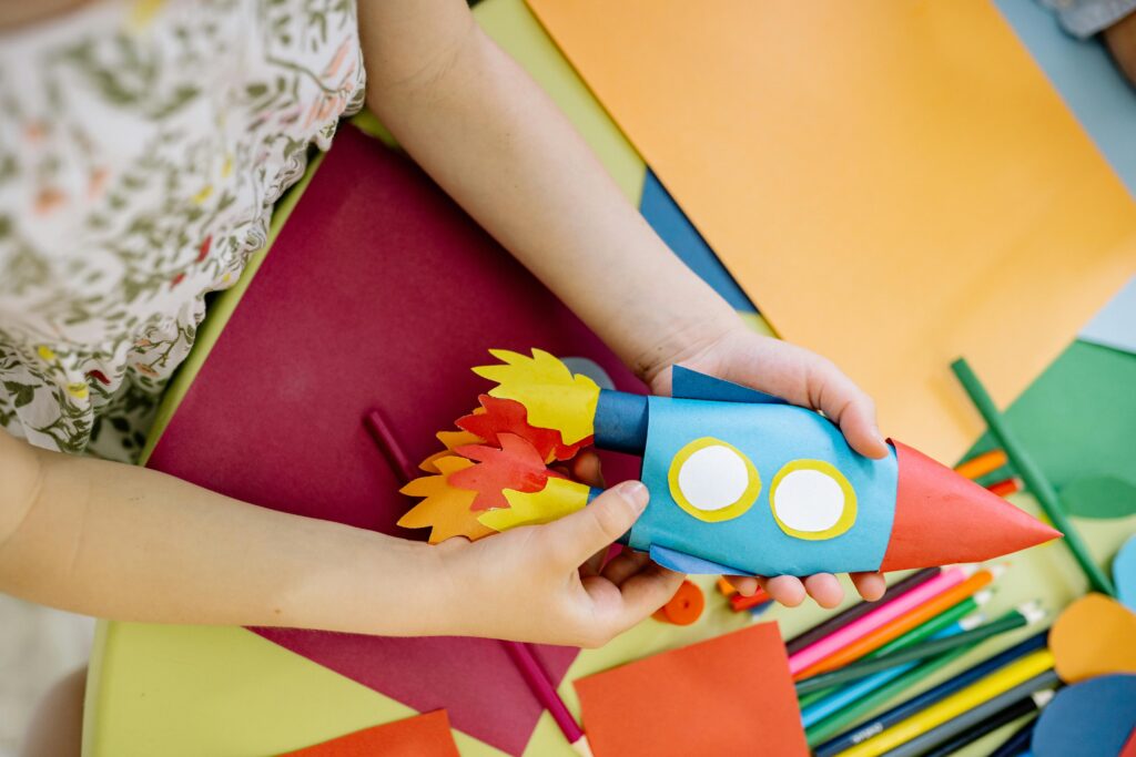Little girl is making a rocket with colored paper